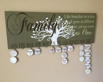 May include: A wooden family calendar with a green background and white tree design. The word "Family" is in a decorative font. It includes months, names, and dates on hanging tags. The quote "Like branches on a tree, we all grow in different directions, yet our roots remain as One."