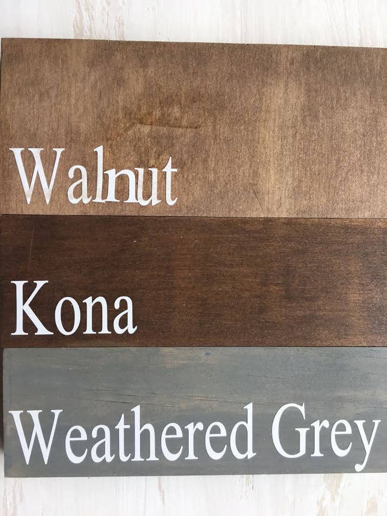 May include: Three wooden planks with different stain colors. The top plank is walnut, the middle plank is Kona, and the bottom plank is weathered gray. Each plank has the color name printed in white.