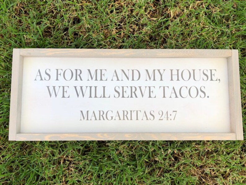 May include: A rectangular wooden sign with a light gray frame, resting on green grass. The sign features the text "AS FOR ME AND MY HOUSE, WE WILL SERVE TACOS. MARGARITAS 24:7" in gray lettering, perfect for a kitchen or dining area.