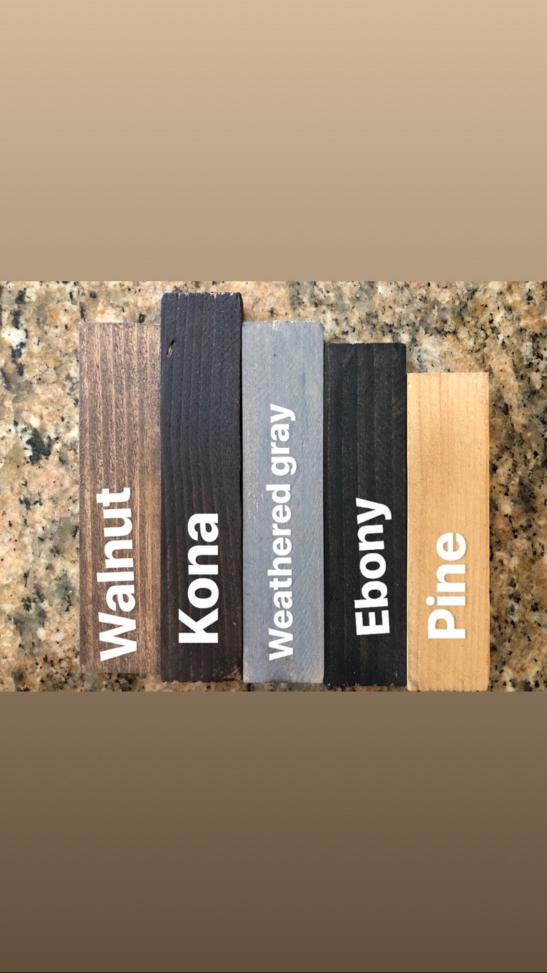 May include: A collection of stained wood samples labeled "Walnut", "Kona", "Weathered gray", "Ebony", and "Pine". The samples are rectangular and vary in color from light brown to black, with the text in white.