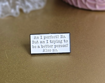 May include: White enamel pin with black text that reads "Am I perfect? No. But am I trying to be a better person? Also no."