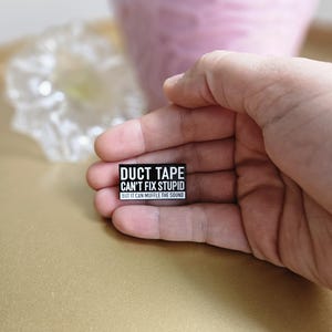 May include: Black and white sticker with the text "Duct Tape Can't Fix Stupid But It Can Muffle The Sound".