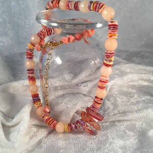 May include: A layered necklace made of pink, orange, and yellow shell beads. The necklace is on a glass surface.