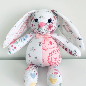 K&ouml;nnte beinhalten: Ein handgemachtes Patchwork-Hasenspielzeug aus Stoffen mit Blumen- und Tiermotiven. Der Hase hat rosa Ohren und eine rosa Schleife. Die Ohren des Hasen sind mit dem Text "AUBREY GABRIEL" und "OCTOBER 21, 2021" personalisiert.