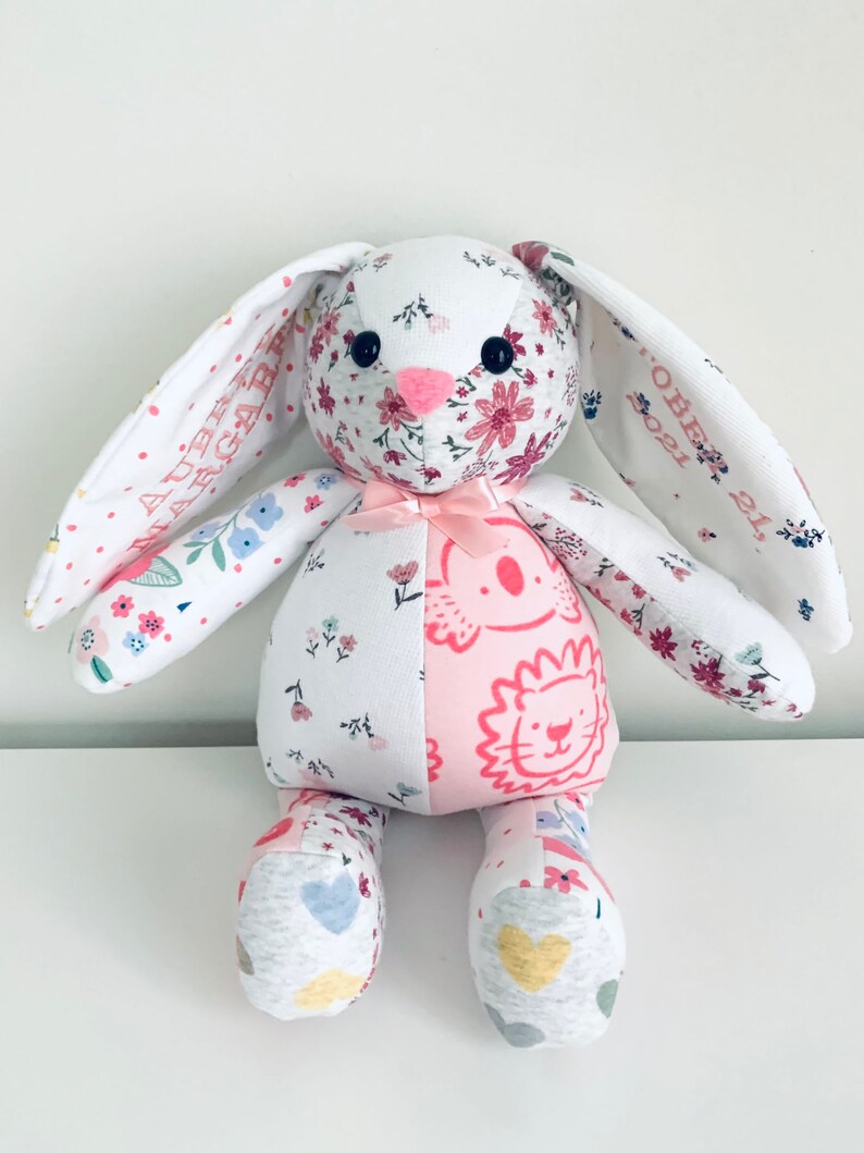 K&ouml;nnte beinhalten: Ein handgemachtes Patchwork-Hasenspielzeug aus Stoffen mit Blumen- und Tiermotiven. Der Hase hat rosa Ohren und eine rosa Schleife. Die Ohren des Hasen sind mit dem Text "AUBREY GABRIEL" und "OCTOBER 21, 2021" personalisiert.