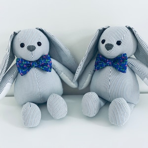 May include: Two gray and white striped plush bunny toys with blue bow ties. The bow ties have a pink flamingo print.