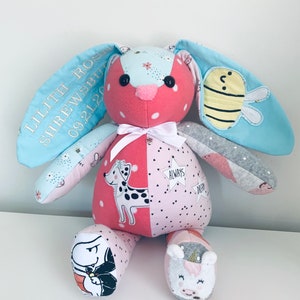K&ouml;nnte beinhalten: Ein rosa-blaues Patchwork-Kuscheltier in Form eines Hasen mit gestickten Details. Der Hase hat eine wei&szlig;e Schleife, schwarze Augen und eine Biene auf einem Ohr. Die Ohren des Hasen sind mit dem Text "Lilith Rose Shrewsbury 09.21.20" bestickt.