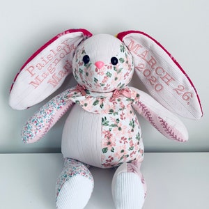 K&ouml;nnte beinhalten: Ein handgemachtes Patchwork-Hasenspielzeug aus rosa Blumenstoff, wei&szlig;em Stoff und rosa Stickerei. Der Hase hat eine rosa Nase und schwarze Augen. Die Ohren sind mit dem Text "Paisley Magnolia March 26, 2020" bestickt.