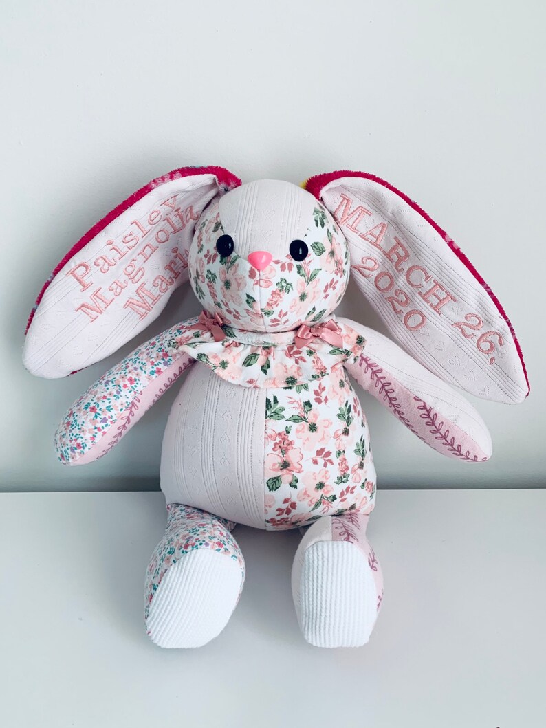 K&ouml;nnte beinhalten: Ein handgemachtes Patchwork-Hasenspielzeug aus rosa Blumenstoff, wei&szlig;em Stoff und rosa Stickerei. Der Hase hat eine rosa Nase und schwarze Augen. Die Ohren sind mit dem Text "Paisley Magnolia March 26, 2020" bestickt.