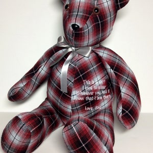 May include: A red, black, and white plaid teddy bear with a silver ribbon around its neck. The bear is embroidered with the text: "This is a shirt I used to wear. Whenever you hold it know that I am there. Love, Dad."