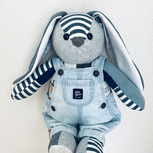 K&ouml;nnte beinhalten: Ein graues und blaues Stofftier-Kaninchen, das eine Jeanslatzhose mit dem Logo "baby bash" tr&auml;gt. Das Kaninchen hat lange, wei&szlig;e Ohren mit schwarz-wei&szlig; gestreiftem Besatz.