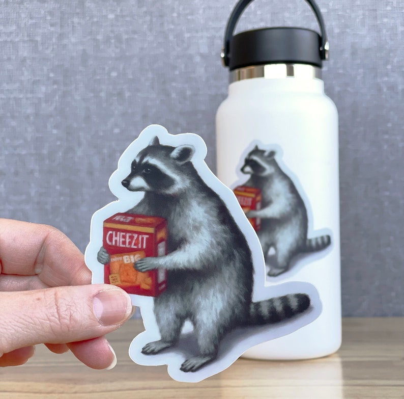 May include: A sticker of a raccoon holding a box of Cheez-It crackers. The sticker is on a white water bottle.