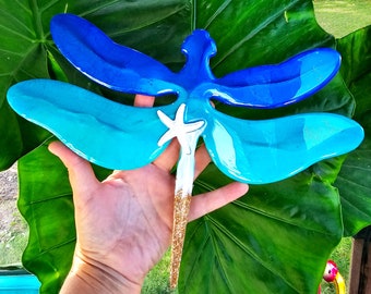 May include: A blue and turquoise dragonfly with a white starfish and gold glitter accents. The dragonfly is made of resin and is a decorative piece for the home or garden.