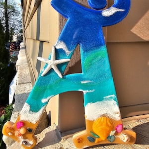 May include: A blue, green, and white resin letter A with a seashell and starfish design. The letter is painted to look like an ocean scene with waves, sand, and seashells.