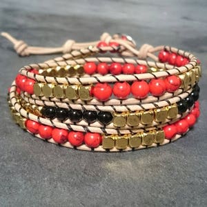 Peut inclure: Un bracelet multi-rangs avec des perles rouges, noires et dorées. Le bracelet est en cuir et a un design enveloppant.