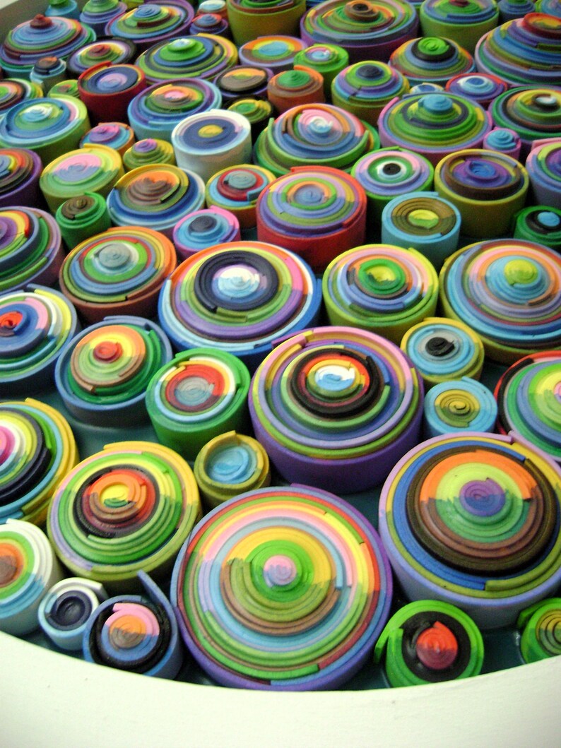 Puede incluir: Primer plano de una obra de arte circular y colorida hecha de anillos conc&eacute;ntricos apilados de papel. Los anillos est&aacute;n dispuestos en un patr&oacute;n aleatorio, creando una superficie visualmente atractiva y texturizada.