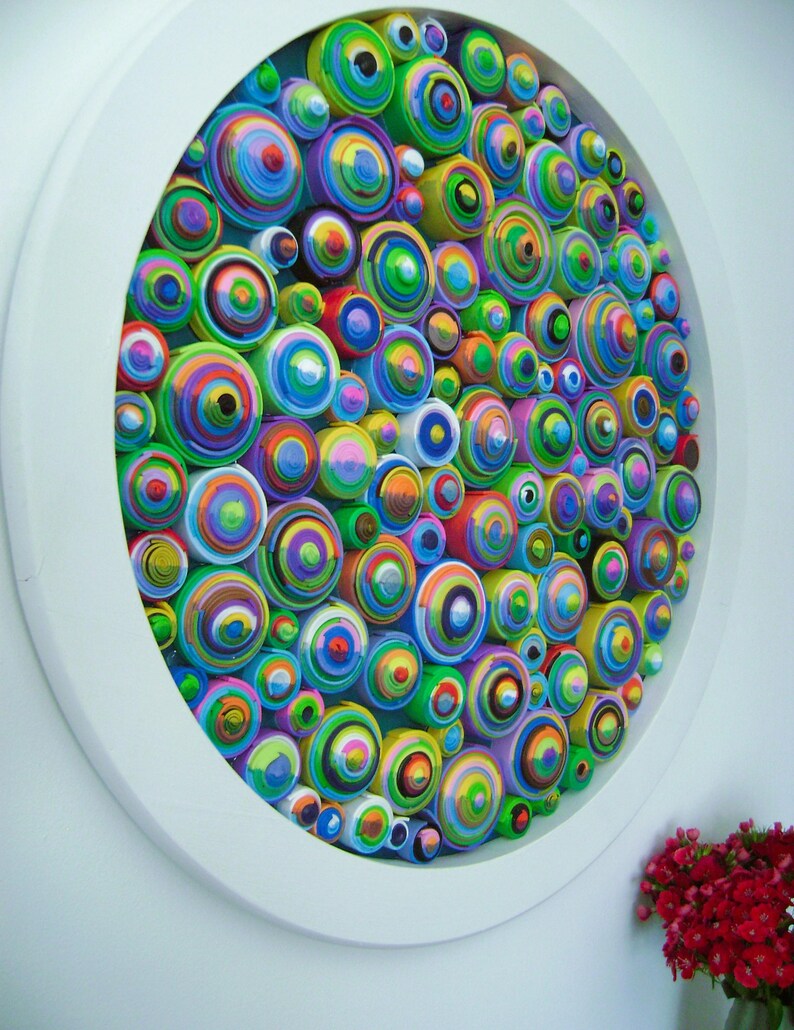 Puede incluir: Una pieza de arte de pared circular hecha de c&iacute;rculos conc&eacute;ntricos coloridos. Los c&iacute;rculos est&aacute;n dispuestos en un patr&oacute;n aleatorio y est&aacute;n pintados en varios tonos de verde, azul, amarillo, rosa y morado.