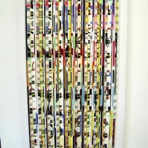 May include: Abstract art piece made of vertical strips of wood painted in various colors and patterns, including black, white, yellow, red, blue, and green.