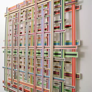 May include: A colorful wall sculpture made of wooden strips, arranged in a grid pattern. The strips are painted in various colors, including red, orange, yellow, green, blue, purple, and black.