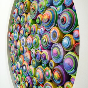 Puede incluir: Una pieza de arte de pared circular hecha de c&iacute;rculos conc&eacute;ntricos de papel de colores. Los c&iacute;rculos est&aacute;n dispuestos en un patr&oacute;n aleatorio, creando un dise&ntilde;o abstracto y visualmente estimulante.