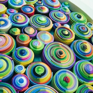 Puede incluir: Primer plano de una obra de arte mural colorida hecha de c&iacute;rculos conc&eacute;ntricos de papel. Los c&iacute;rculos est&aacute;n dispuestos en un patr&oacute;n aleatorio y est&aacute;n en varios tonos de azul, verde, amarillo, rojo y morado.