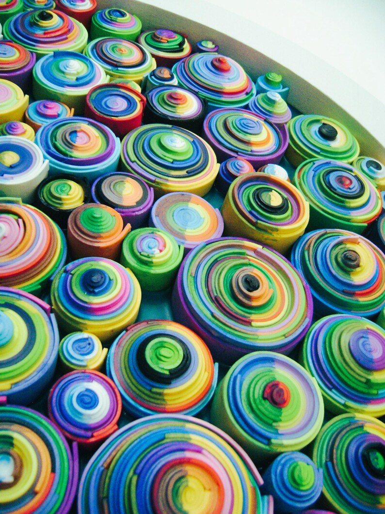 Puede incluir: Primer plano de una obra de arte mural colorida hecha de c&iacute;rculos conc&eacute;ntricos de papel. Los c&iacute;rculos est&aacute;n dispuestos en un patr&oacute;n aleatorio y est&aacute;n en varios tonos de azul, verde, amarillo, rojo y morado.