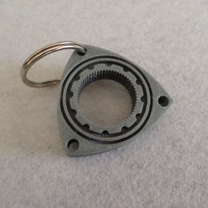 May include: A gray 3D printed keychain shaped like a rotary engine with a silver key ring.