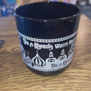 May include: Black glass tumbler with white text and illustrations. The text reads "Do a Kahlua White Russian". The design includes images of onion dome buildings. A beverage glass.