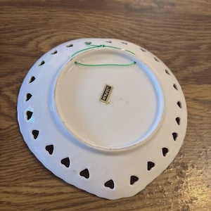 May include: White ceramic decorative plate with heart-shaped cutouts around the edge. A green string is attached for hanging. The plate has a sticker that reads "JAPAN".