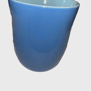 May include: A blue ceramic vase with a curved, asymmetrical shape. The exterior is a solid, glossy blue, while the interior has a lighter blue hue. The vase has a smooth, polished finish.