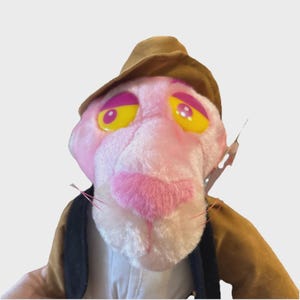 Può includere: Un peluche della Pantera Rosa con cappello e giacca marroni. La pantera ha pelliccia rosa, naso rosa e occhi gialli con dettagli viola. Un giocattolo da collezione vintage.
