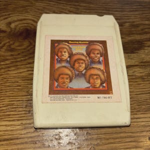 May include: An off-white 8-track tape cartridge featuring the album "Dancing Machine" by The Jackson 5. The album art shows five men with brown afro hairstyles. The tape has the Motown Records logo.