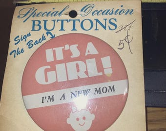 May include: Vintage "It's a Girl!" button on its original card. The button is pink with white text and a baby graphic. The card reads "Special Occasion Buttons" and "Sign the Back."