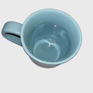 May include: A light blue ceramic mug with a curved handle. The mug is empty and viewed from above, showing the interior. The mug's interior and exterior are the same color. The mug is on a white background.