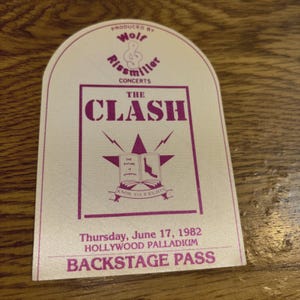 May include: A vintage backstage pass for The Clash concert, featuring a cream-colored background with purple text. The pass includes the band's name, concert details, and the phrase "KNOW YOUR RIGHTS". The pass is from the Hollywood Palladium.