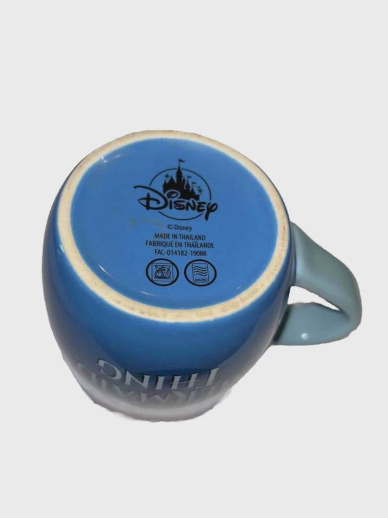 May include: Blue ceramic Disney mug with a light blue handle. The bottom of the mug features the Disney logo and text that reads "MADE IN THAILAND". The mug has the words "SOMETHING" and "MAGIC" printed on the side.