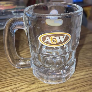 May include: A white ceramic mug with a black handle and the text "But First, Coffee" in a bold, black font. The mug is sitting on a wooden surface. The mug appears to be 12 ounces.