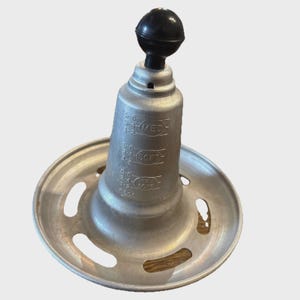 May include: A vintage silver-toned metal food mill with a black knob on top. The mill has a flared base with several oval cutouts and a cylindrical body with measurements labeled "MED" and "SOFT".