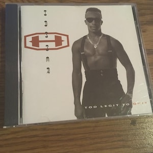 May include: A CD case featuring the album "Too Legit to Quit" by Hammer. The cover art displays Hammer in sunglasses and suspenders. The album title and artist name are prominently displayed in red and black.