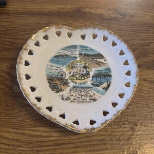 May include: Heart-shaped decorative plate with a gold rim and heart-shaped cutouts. The center features a colorful illustration of Wildwood, New Jersey, with text that reads "Wildwood by the Sea" and "New Jersey."
