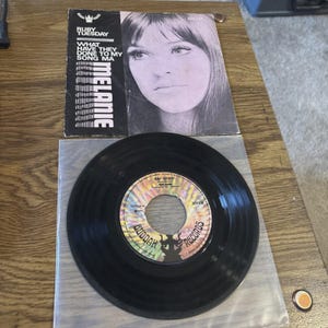 May include: A 7-inch vinyl record by Melanie featuring the songs Ruby Tuesday and What Have They Done To My Song Ma. The record sleeve displays a black and white portrait of the artist, while the record label features a colorful sunburst design.