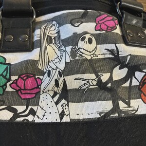 Puede incluir: Bolso tote a rayas blancas y negras con Sally y Jack Skellington de Pesadilla antes de Navidad. El bolso tiene asas y ribetes negros, con detalles de rosas de colores. El bolso est&aacute; hecho de un material de lona duradero.