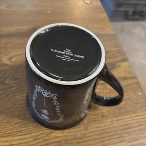 May include: Black ceramic mug featuring a design from "The Nightmare Before Christmas." The mug has a white rim and handle. The bottom of the mug has text that reads "The Nightmare Before Christmas" and "Dishwasher and Microwave Safe."