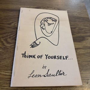 Op de afbeelding: Een klein boekje met een beige omslag met een zwarte lijntekening van een gezicht en de tekst "Think of Yourself..." door Leon Saulter. Het boekje wordt bij elkaar gehouden met nietjes.