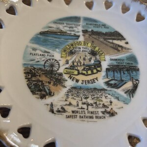 May include: A white decorative plate with a detailed illustration of Wildwood, New Jersey. The design includes a Ferris wheel, beach scenes, and text that reads "Wildwood by the Sea" and "World's Finest, Safest Bathing Beach."