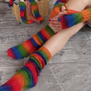 Può includere: Un paio di calze a righe arcobaleno e guanti senza dita abbinati. Le calze sono lunghe e hanno una trama a coste. I guanti sono senza dita e hanno un motivo a righe simile.