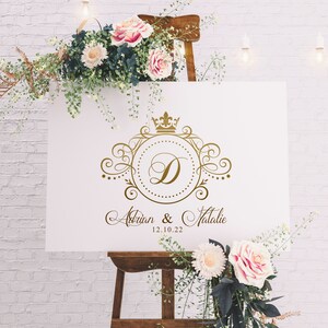 May include: White wedding sign with a gold ornate design featuring a crown and the letter D. The sign reads "Adrian & Natalie 12.10.22".