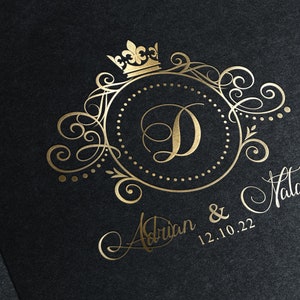 May include: Gold wedding invitation with a decorative monogram featuring the letter D, a crown, and ornate scrollwork. The names Adrian & Natalie and the date 12.10.22 are written in cursive.