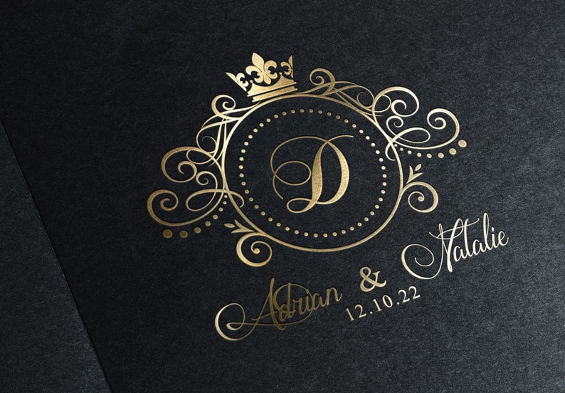 May include: Gold wedding invitation with a decorative monogram featuring the letter D, a crown, and ornate scrollwork. The names Adrian & Natalie and the date 12.10.22 are written in cursive.