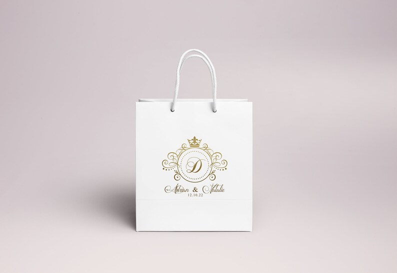 May include: White paper gift bag with a gold crown and the letter D in a circle. The text "Alison & Natalie 12.18.22" is printed below the logo.